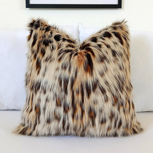 Luxury Leopard Cat faux fur pillow cover with ultra-soft long pile in natural cream, caramel, brown and charcoal tones styled on a white bed.