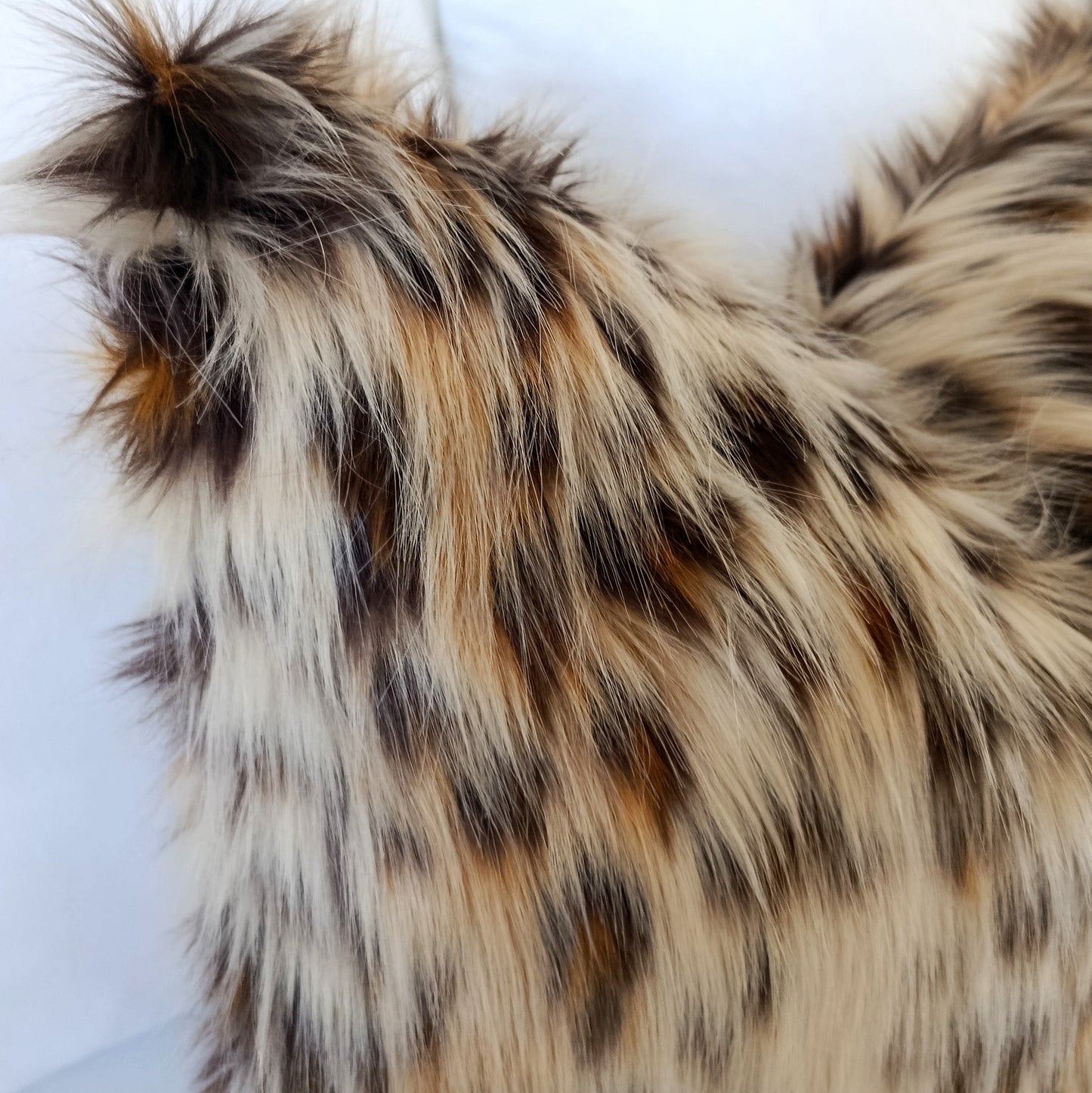 Luxury Leopard Cat faux fur pillow cover with ultra-soft long pile in natural cream, caramel, brown and charcoal tones styled on a white bed.